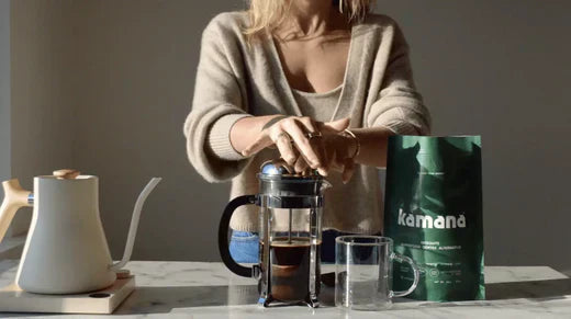 Mesquite coffee alternative from Kamana being brewed in a French press with a kettle and glass mug on a marble countertop