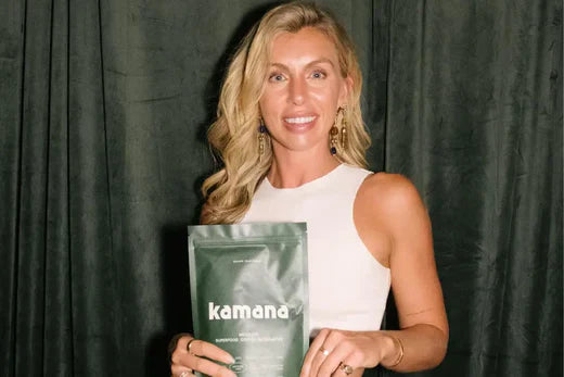 Coffee alternative brand Kamana held by a smiling woman in a white dress against a dark curtain background