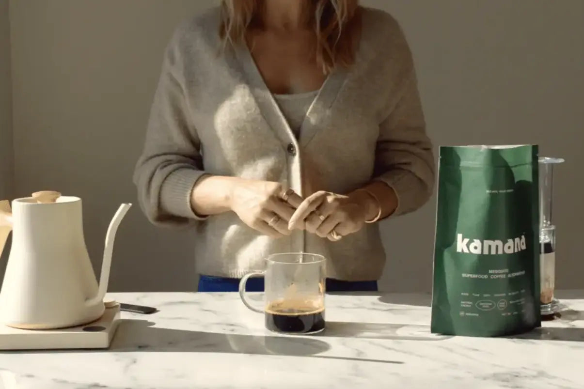 Coffee substitute brewed and served in a glass mug alongside a bag of Kamana mesquite coffee and a gooseneck kettle