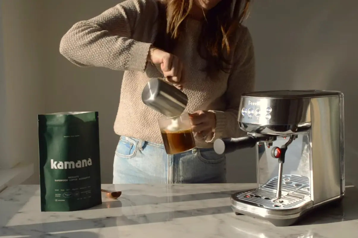 Non-caffeine drinks being prepared with steamed milk poured into a glass of mesquite coffee beside an espresso machine.